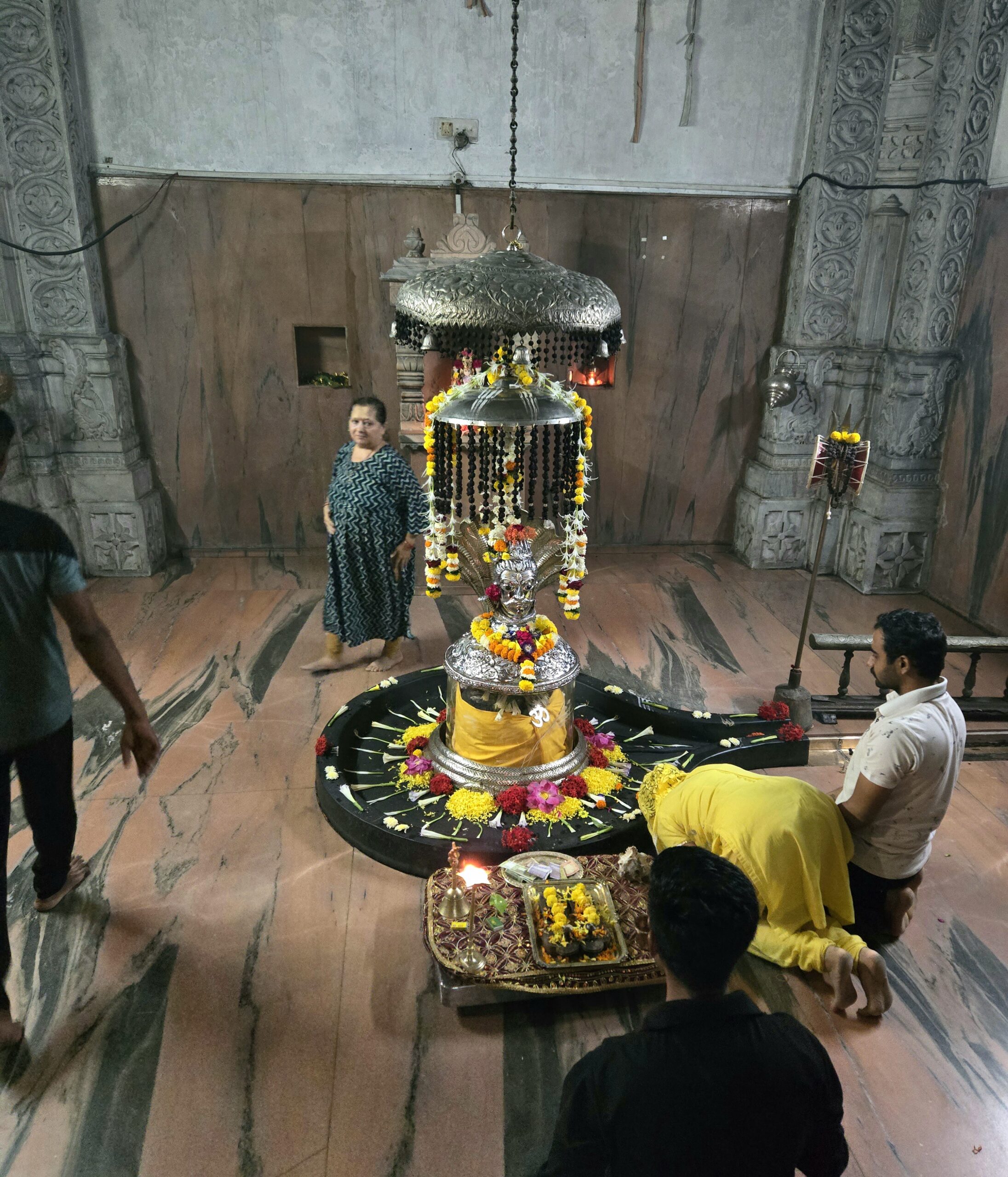 Devotees praying before the flower-decorated Shiva linga beneath a silver canopy