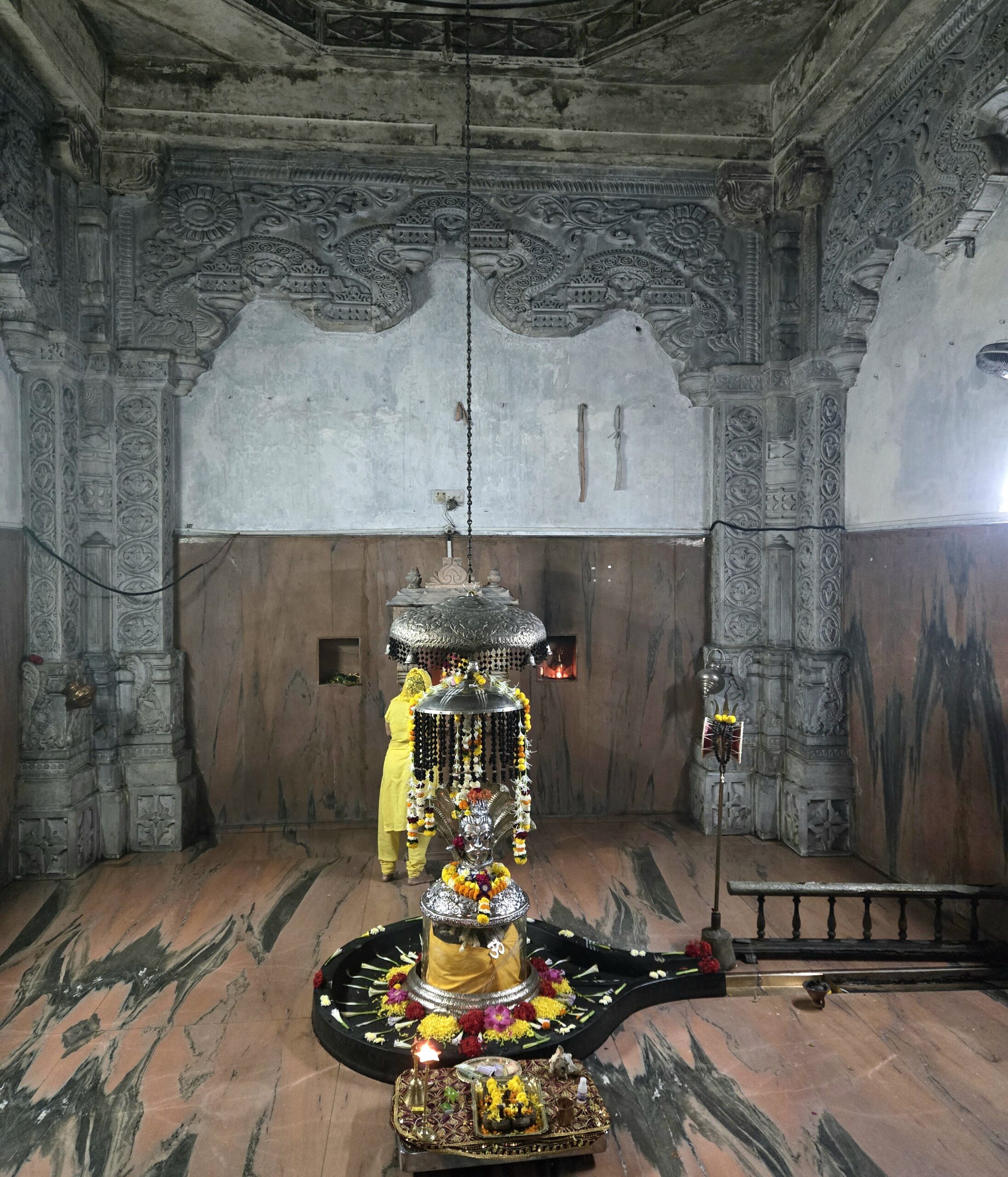 Decorated Shiva linga framed by carved gray stone pillars inside the nighttime temple