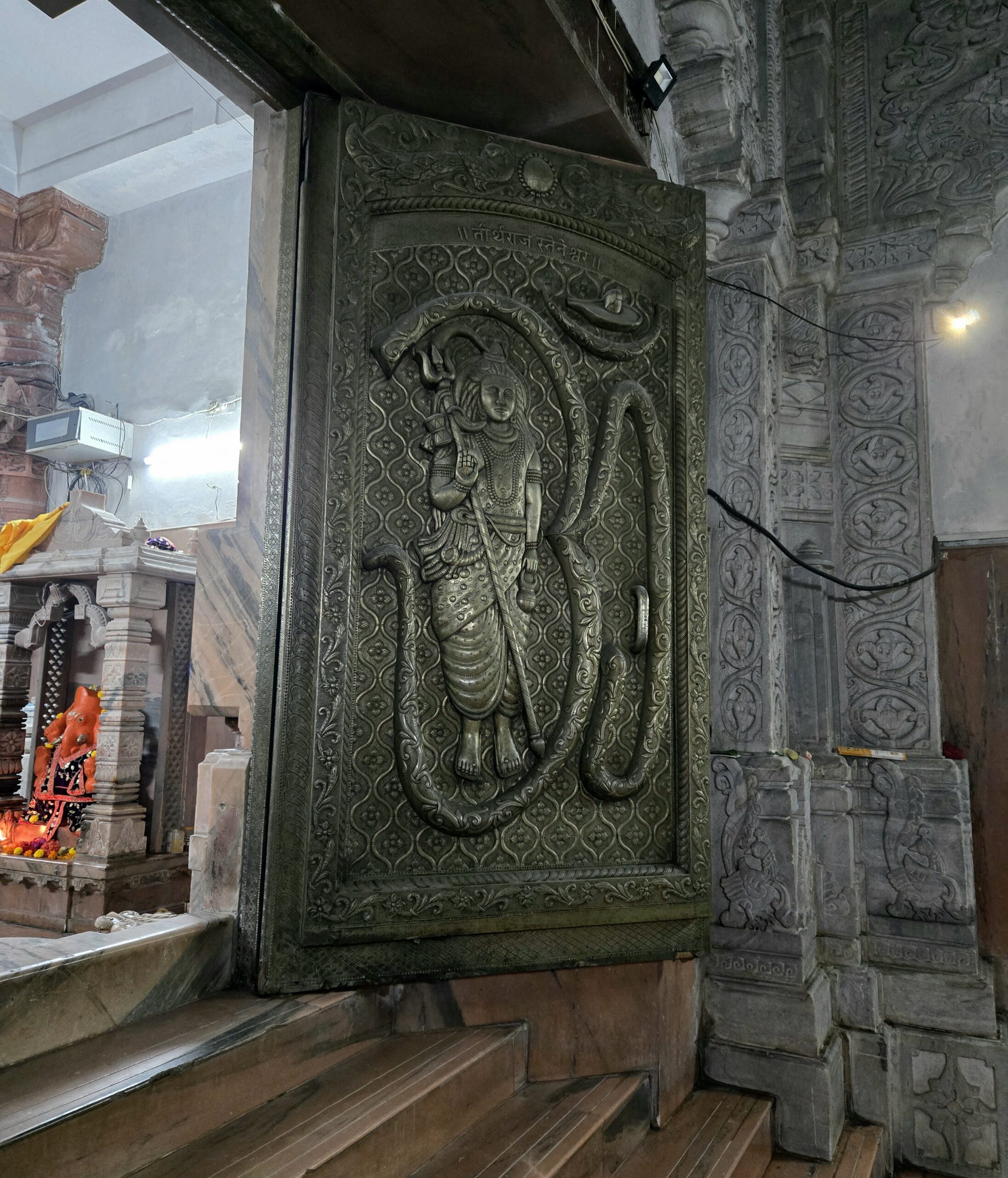 Detailed carved door panel depicting Shiva Bhagwan with a trishul inside the stone temple